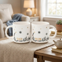 Sophisticated matching 'Dad and Mom' ceramic coffee mug set with elegant gold text, winter holly and snowflake design, perfect as a cozy holiday gift for parents, displayed in a minimalist home living room setting