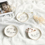 A set of white ceramic Skyline Jewelry Dishes featuring minimalist Chicago, Dallas, and Philadelphia skyline sketches with gold rims, styled on soft lace with delicate accessories.