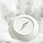 The underside of a white ceramic Skyline-Jewelry-Dish, featuring the Collective Home brand logo, displayed on a soft, white textured fabric background.