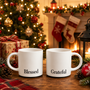 A festive Christmas gift set featuring the Black Blessed & Grateful Mug Set, displayed on a wooden table with seasonal ornaments, glowing tree lights, and cozy fireplace decor.